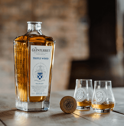 The Glenturret Triple Wood Single Malt Whisky 700ml bottle with two glasses on a wooden table, showcasing its rich color and craftsmanship.