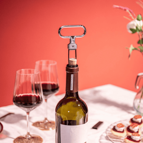 Vacu Vin Cork Puller Stainless Steel opening wine bottle with two wine glasses and appetizers in background