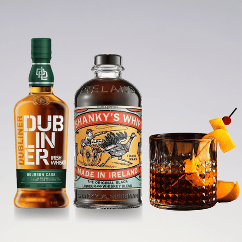 Bottles of Dubliner Irish Whiskey and Shanky's Whip Liqueur beside a cocktail glass garnished with an orange twist and cherry.