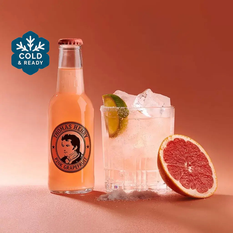 Thomas Henry Pink Grapefruit Tonic 200ml bottle with glass of ice and lime on a pink background, showcasing refreshing premium mixer.