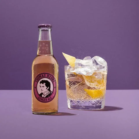 Thomas Henry Ginger Ale 200ml bottle with cocktail in glass, clear amber color, on a purple background.